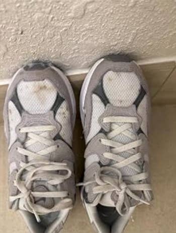 A pair of stained sneakers on a tiled floor against a wall