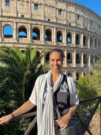 Person smiling in front of the Colosseum, wearing a floral-patterned top with a light scarf