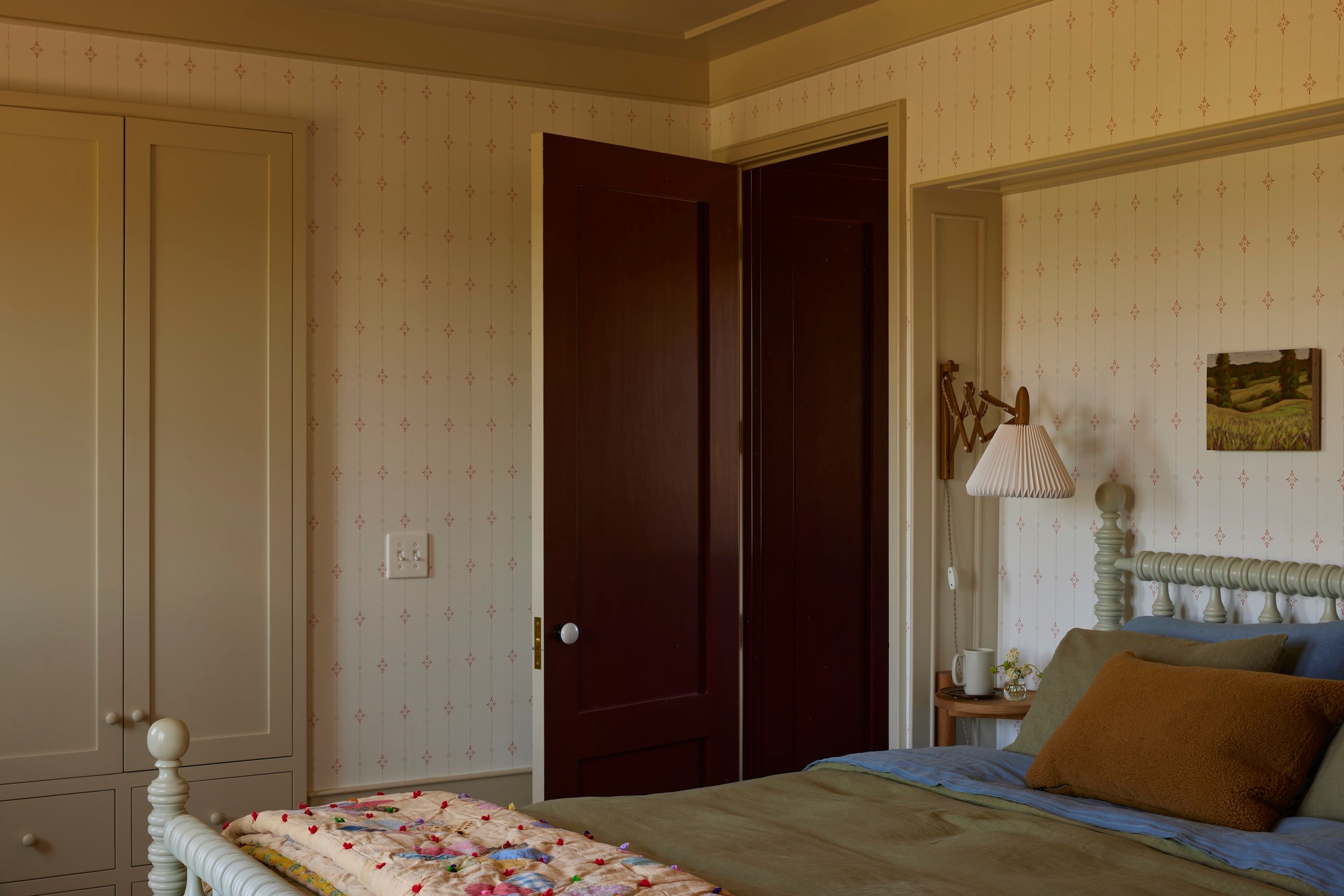 In the guest bedroom, a ’70s wallpaper, Kelapa in ruby red, plays off linen bedding by Once Milano, sheep vice versa cushions in Havane by Cedar & Hyde Mercantile, and a vintage floral hand-tied Dresden plate quilted bedspread (circa 1940s) from 86 Vintage. Bedside Rim table by Summer Studio. Plug-in sconce is Le Klint Sax in smoked oak via Finnish Design Shop.