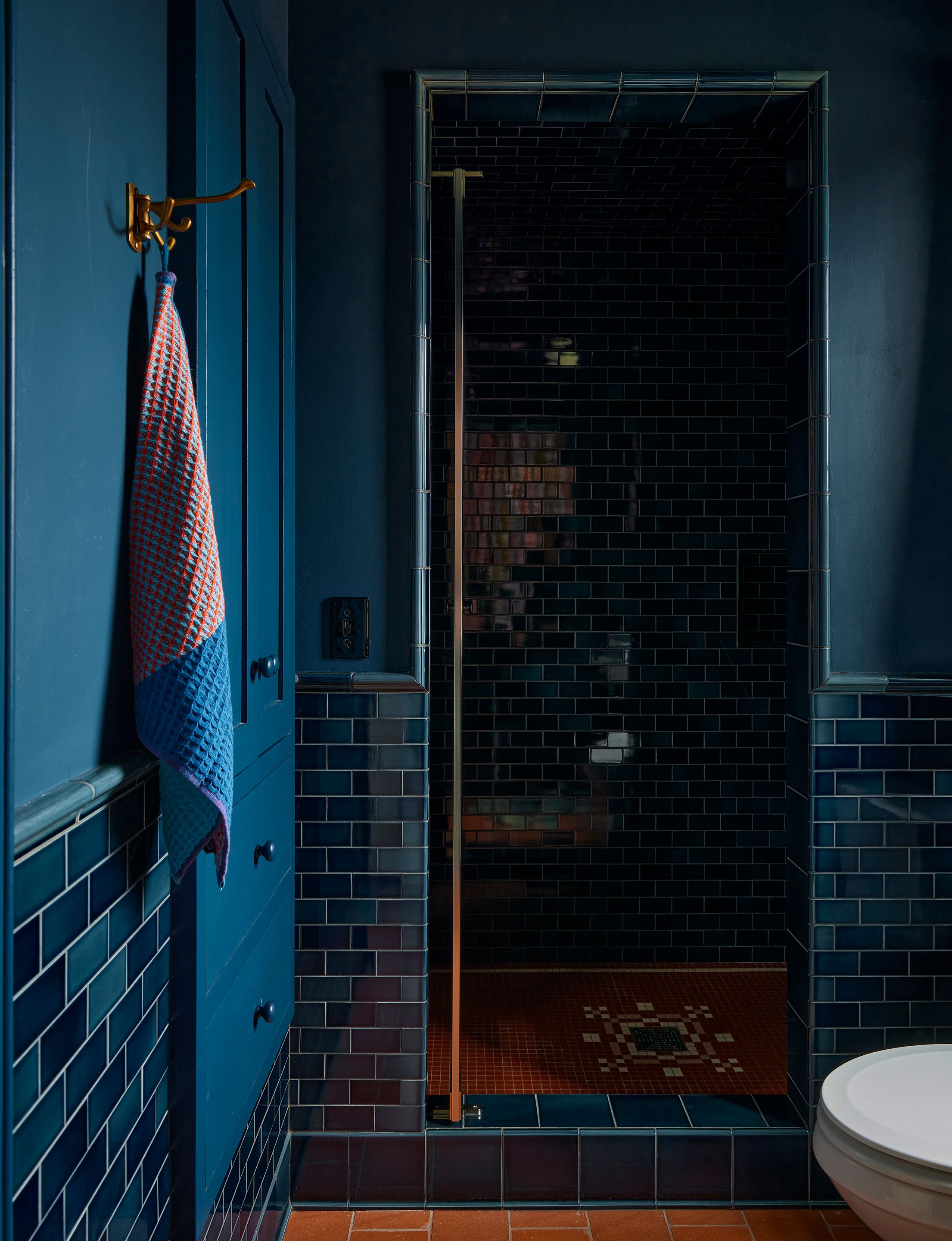 In the guest bathroom, the terracotta tile floors, Subway Ceramics tile wainscot, and custom shower basin mosaic continue the look of the primary house bathrooms. The swing hook is by van Cronenburg. The waffle towel in red moon is Lateral Objects.