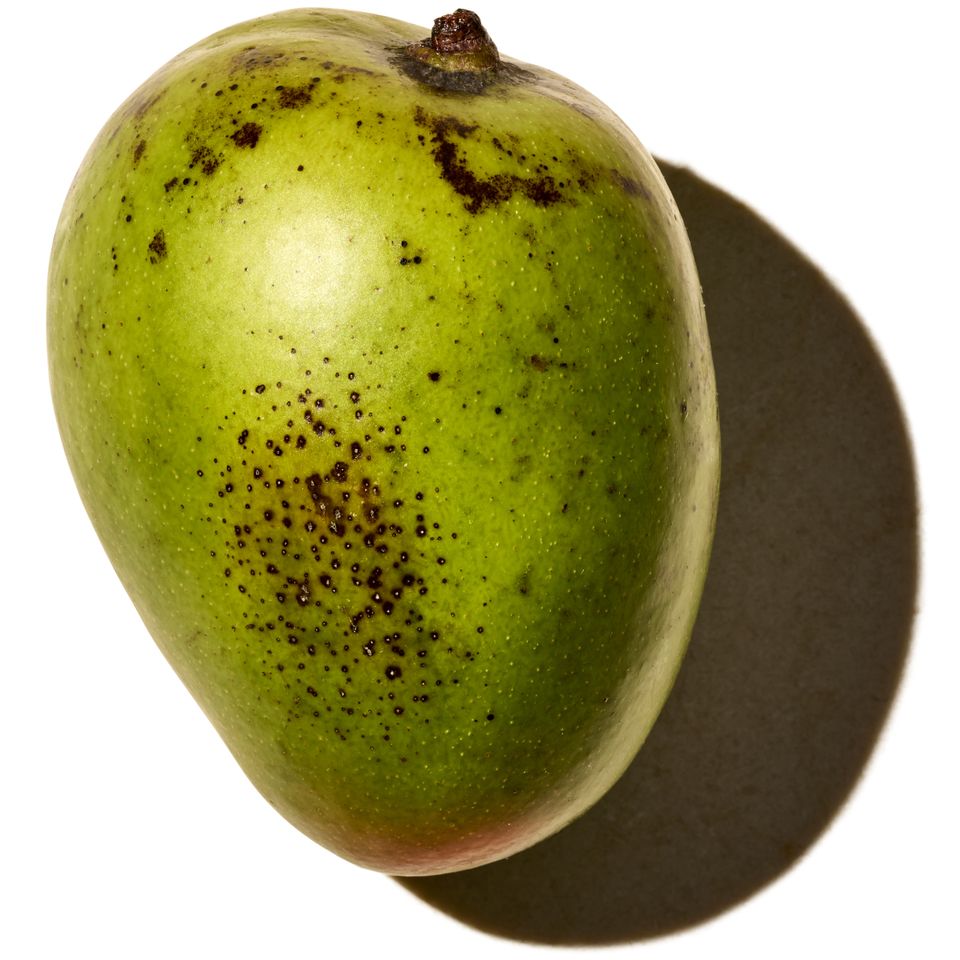 A ripe mango with dark spots on its skin and a shadow cast to one side