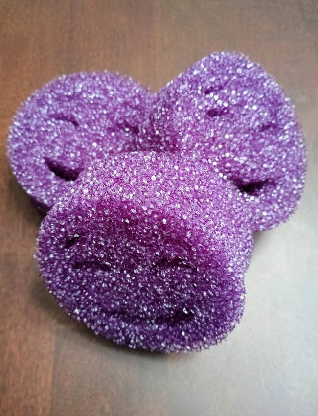 Three purple textured scrub pads arranged overlapping each other on a wooden surface