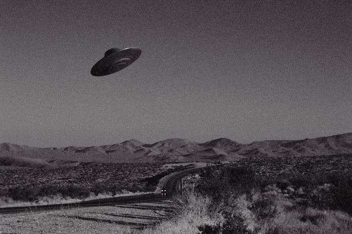 A UFO flies over a deserted, winding road in a barren landscape, evoking mystery and intrigue