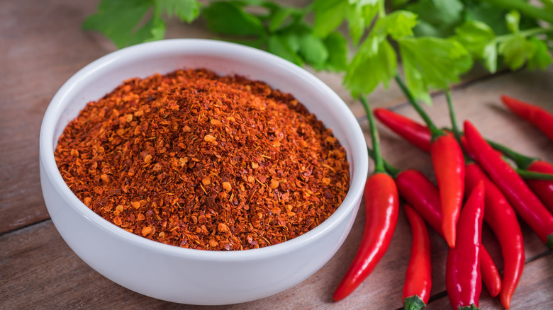 A bowl of ground cayenne pepper next to fresh chilli peppers
