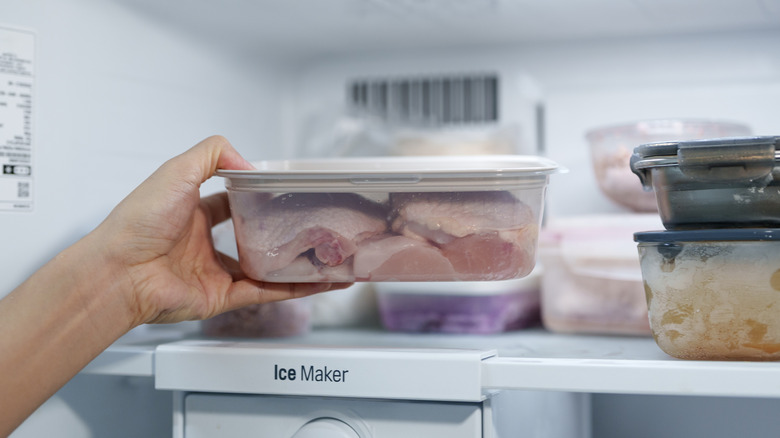 Person placing a container of raw chicken inside a refrigerator near the ice maker.