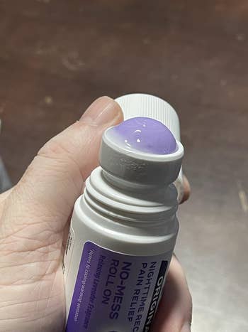 Person holding a no-mess roll-on pain relief applicator, dispensing a gel