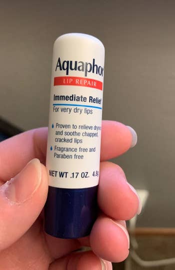 Hand holding Aquaphor Lip Repair tube for very dry lips, providing immediate relief, fragrance-free, and paraben-free, 0.17 oz