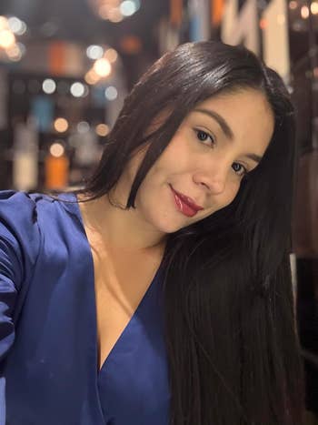 reviewer with long hair poses in a silky blouse with a V-neckline. She smiles slightly, creating a stylish and elegant look