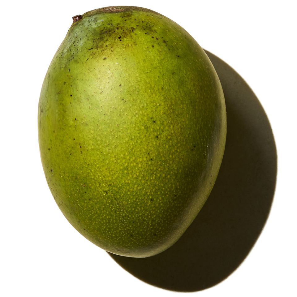 A whole mango placed on a white background with its shadow visible