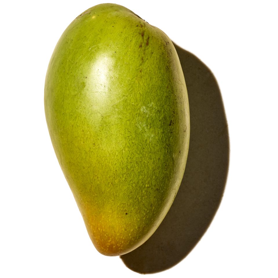 A mango placed against a white background with a shadow visible to the side