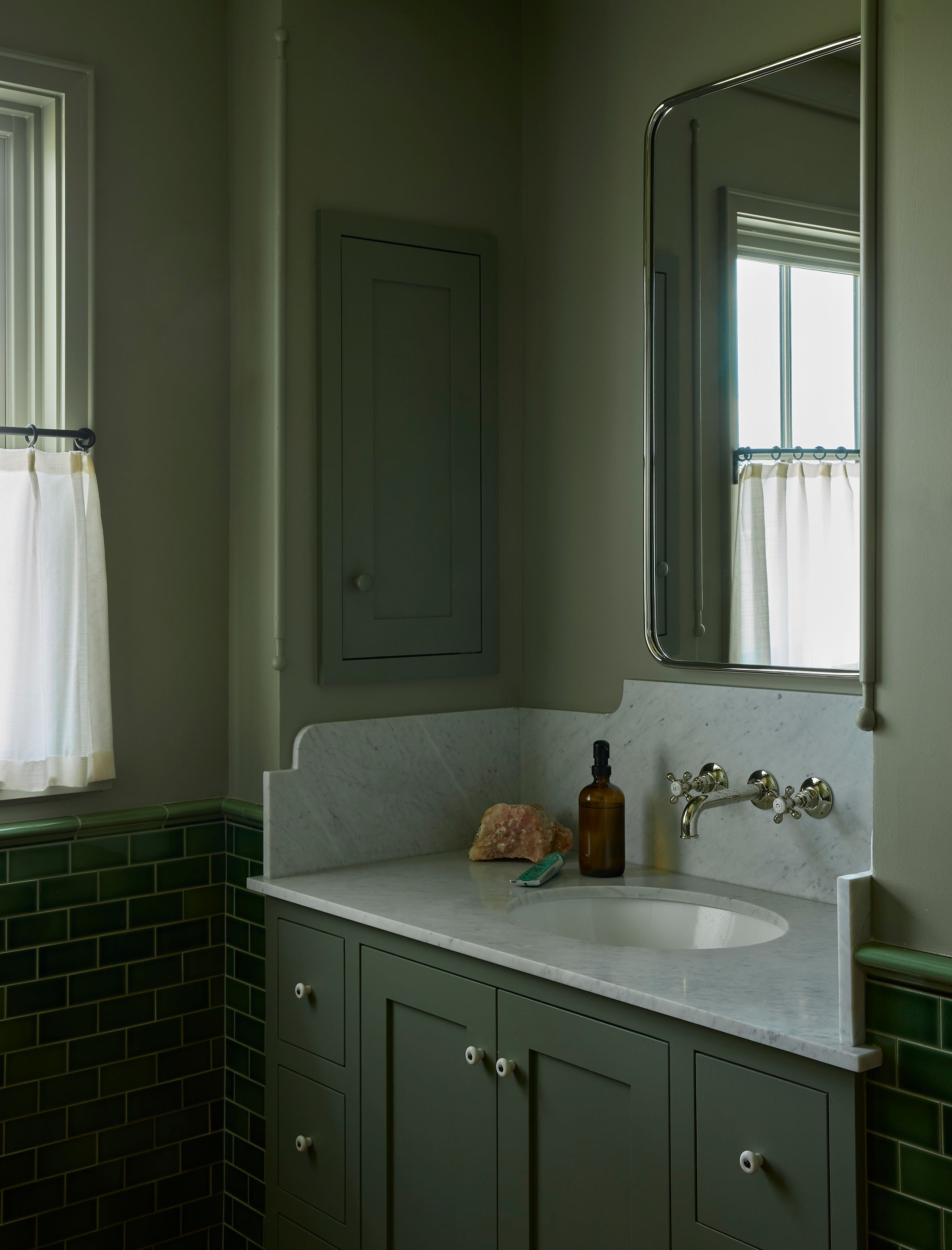 In the kids’ bathroom, the lichen walls (Farrow & Ball) are met by a wainscot in Subway Ceramics Crackle Hunter green tile. The sink and backsplash are Bianco Carrara Honed by Arizona Tile. The highgate wall-mounted faucet with cross handles in nickel is Waterworks.