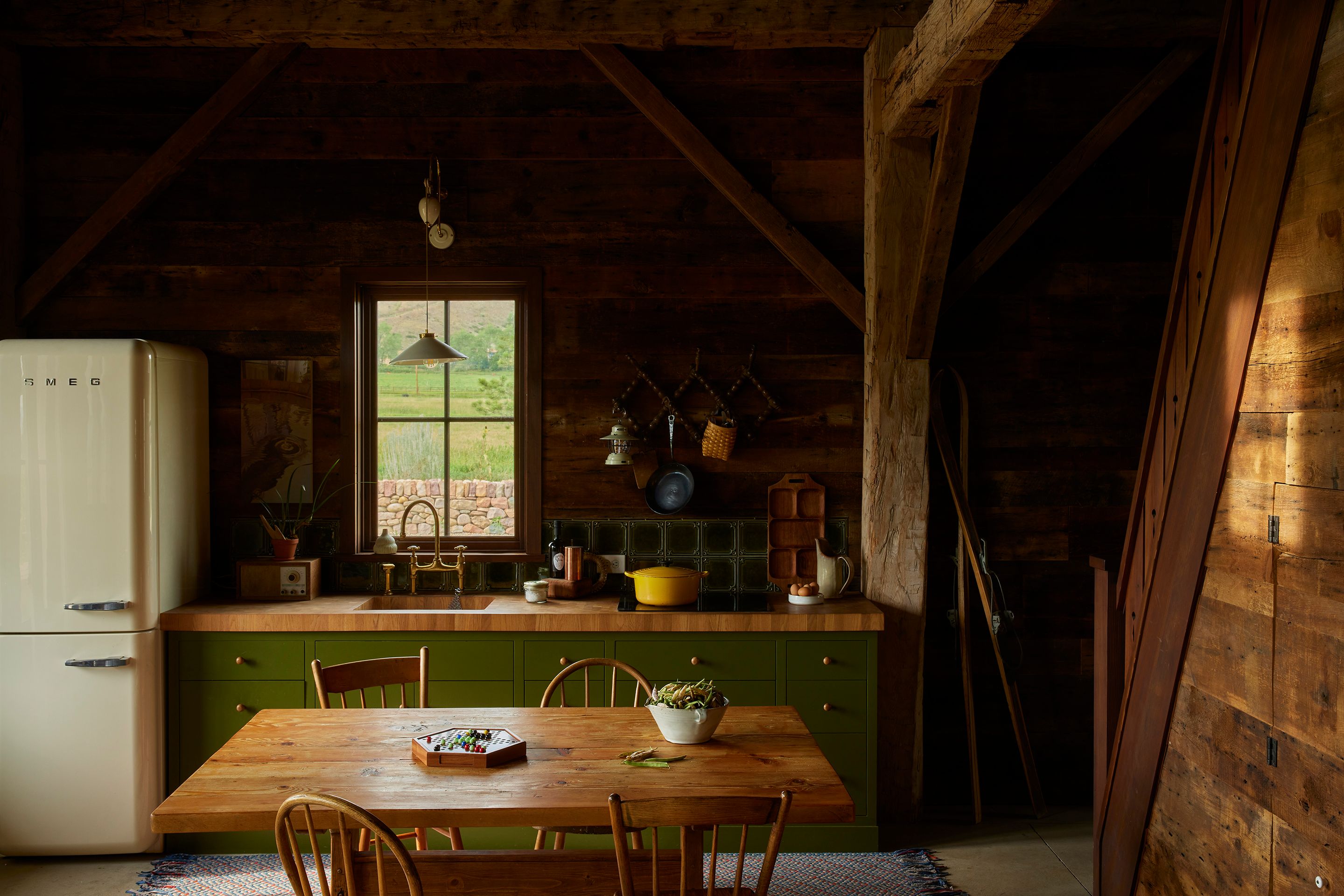 The visible timber frame was once an old barn that Coburn Partners sourced from Heritage Restorations and engineered for use inside the guest cabin. The walls are covered in reclaimed naily board. The refrigerator is Smeg. The countertops, white-oak end-grain butcher block, are from Armani Fine Woodworking. The tile backsplash is Champetre Blanc in Limerick by Rookwood.