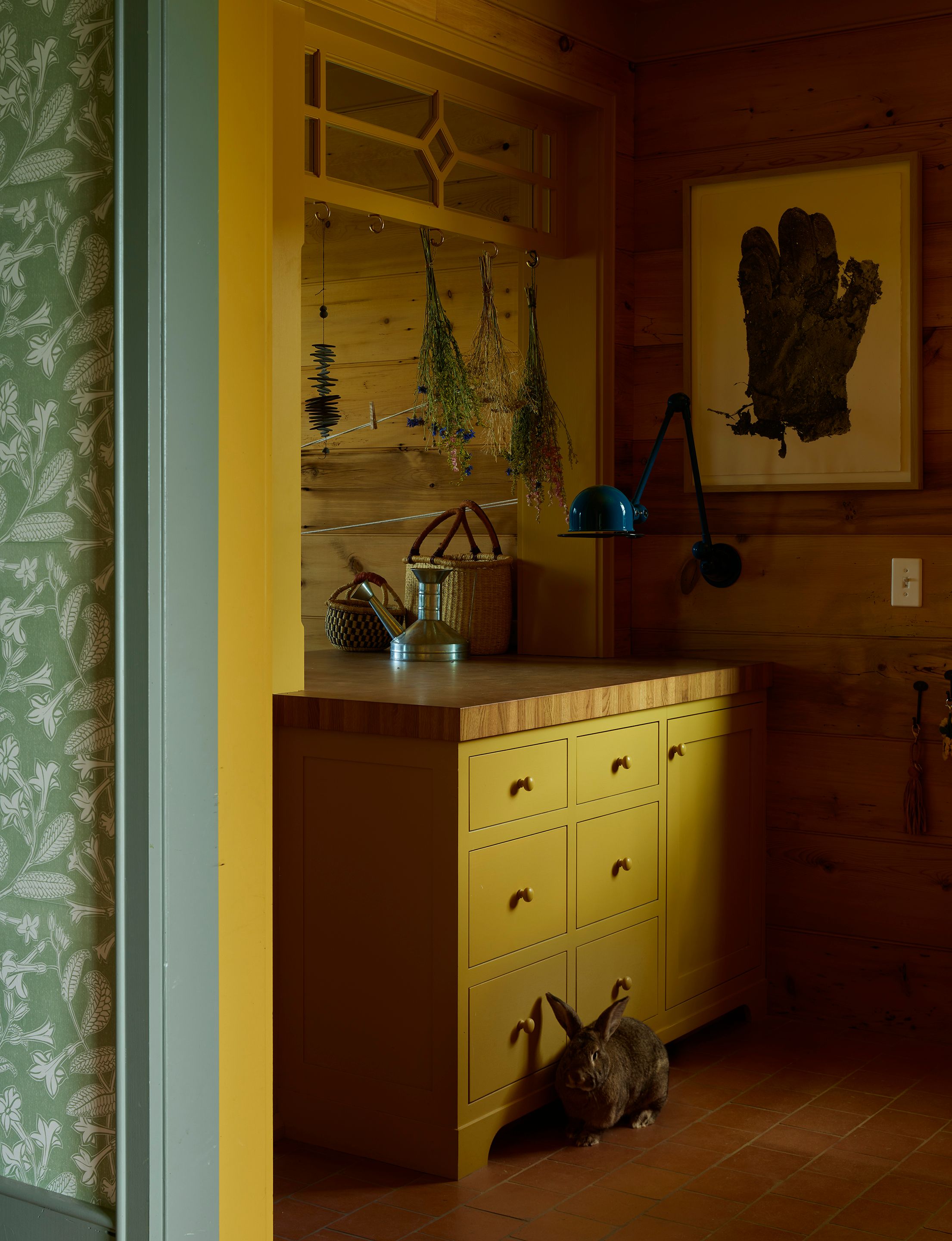 The intent for the pine walls in the mudroom was paint, but everyone fell in love with the look of the wood during construction, so it was given a clear coat and left as is. The molding and transom (custom by Landed) are India yellow by Farrow & Ball. Irving Penn’s Mud Glove hangs near a Loft sconce in ocean blue from Jieldé.