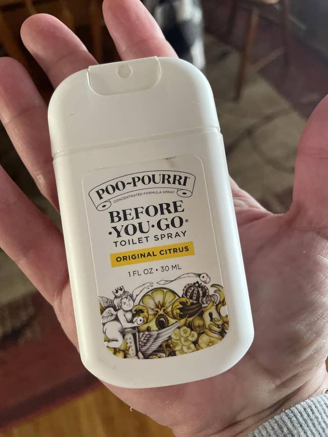 Person holding a small bottle of Poo-Pourri Original Citrus toilet spray