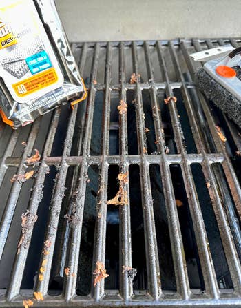 Grill grate with char marks, a grill cleaning pad, and a package of grill cleaning wipes, highlighting cleaning tools for BBQ maintenance