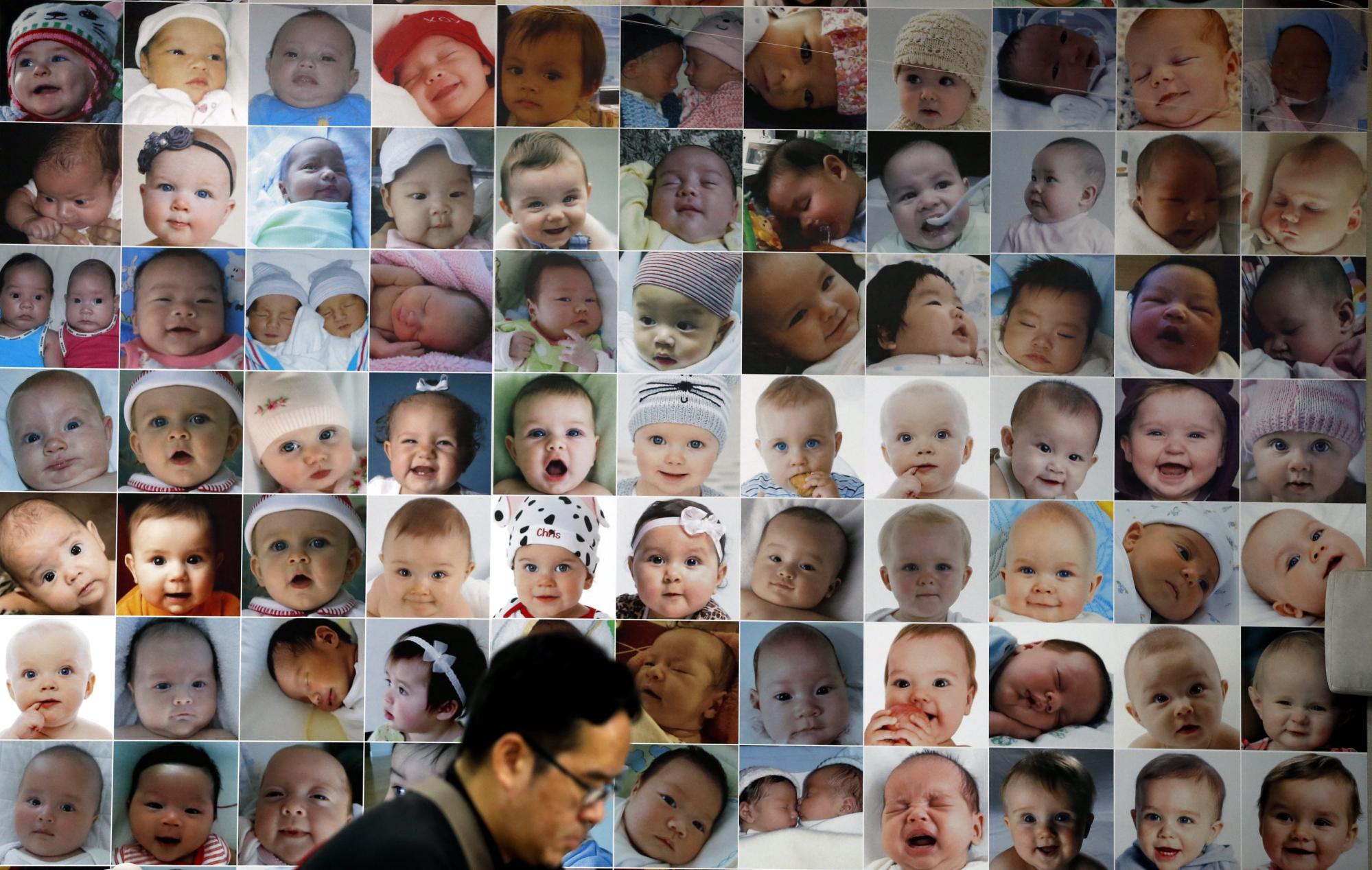 A man uses his mobile phone as he walks past portraits of babies used as advertisement for a fertility clinic in Bangkok. Photo: EPA
