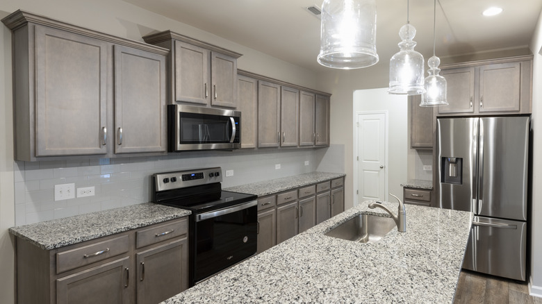 Kitchen with white walls, muted brown wood cabinets, gray granite counters, and black and steel appliances