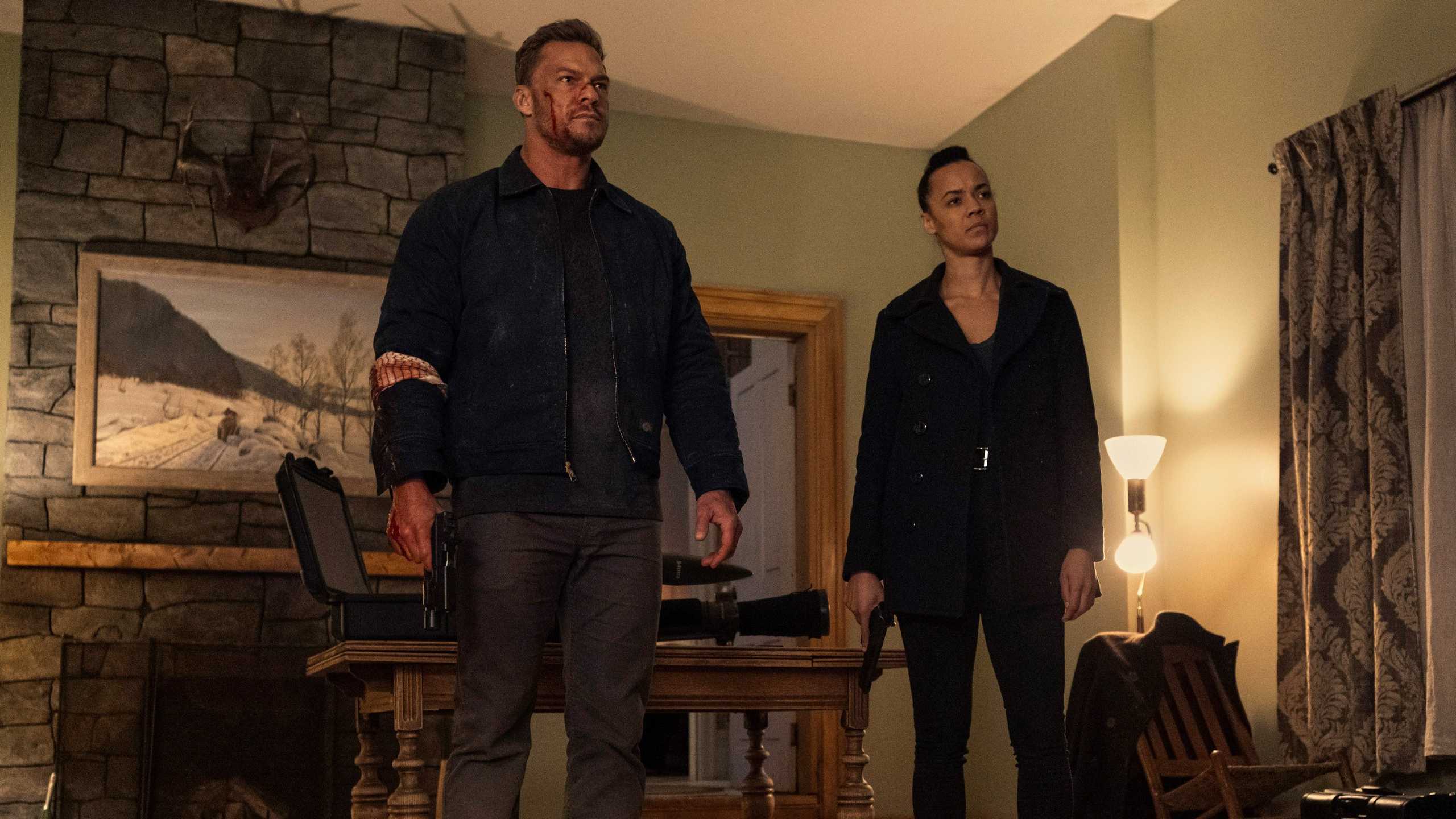 Reacher (Alan Ritchson) and Neagley (Maria Sten) standing together inside a house in Reacher