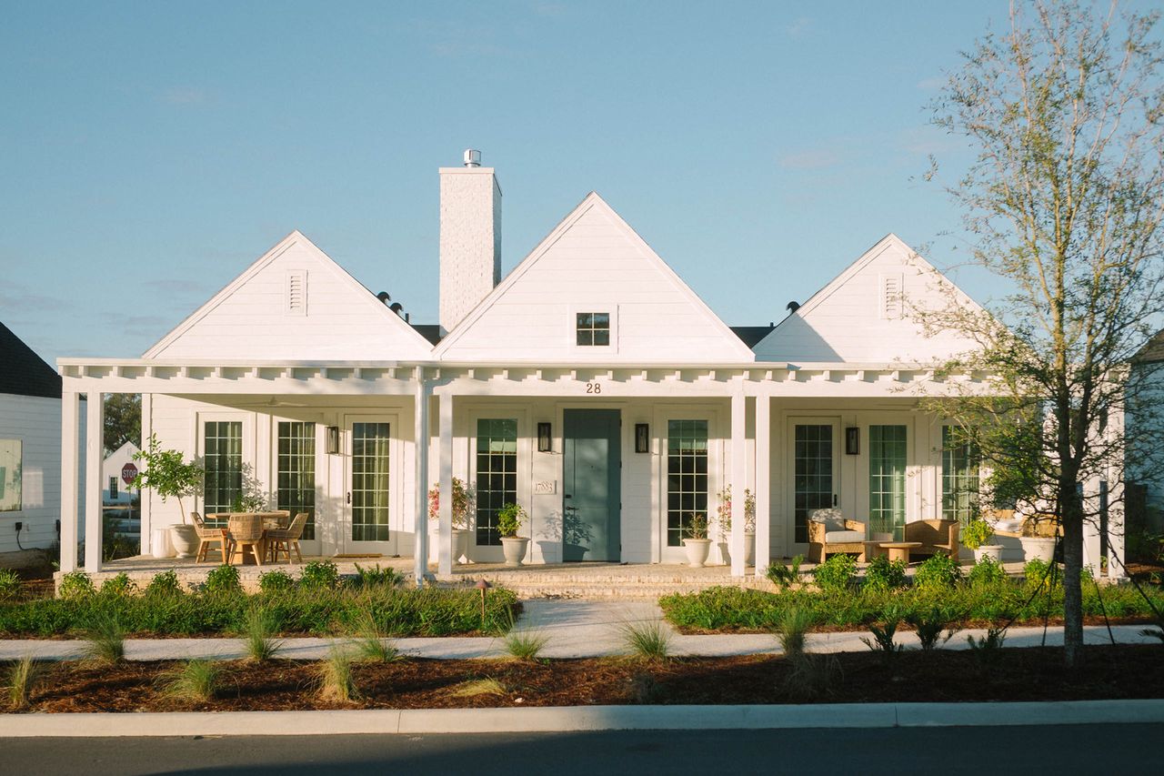 A white house with a front veranda and multiple entrance doors surrounded by landscaped greenery