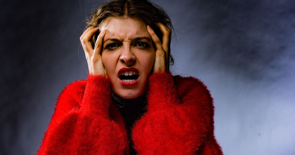 A woman in a red sweater expressing anger and frustration in a studio portrait.