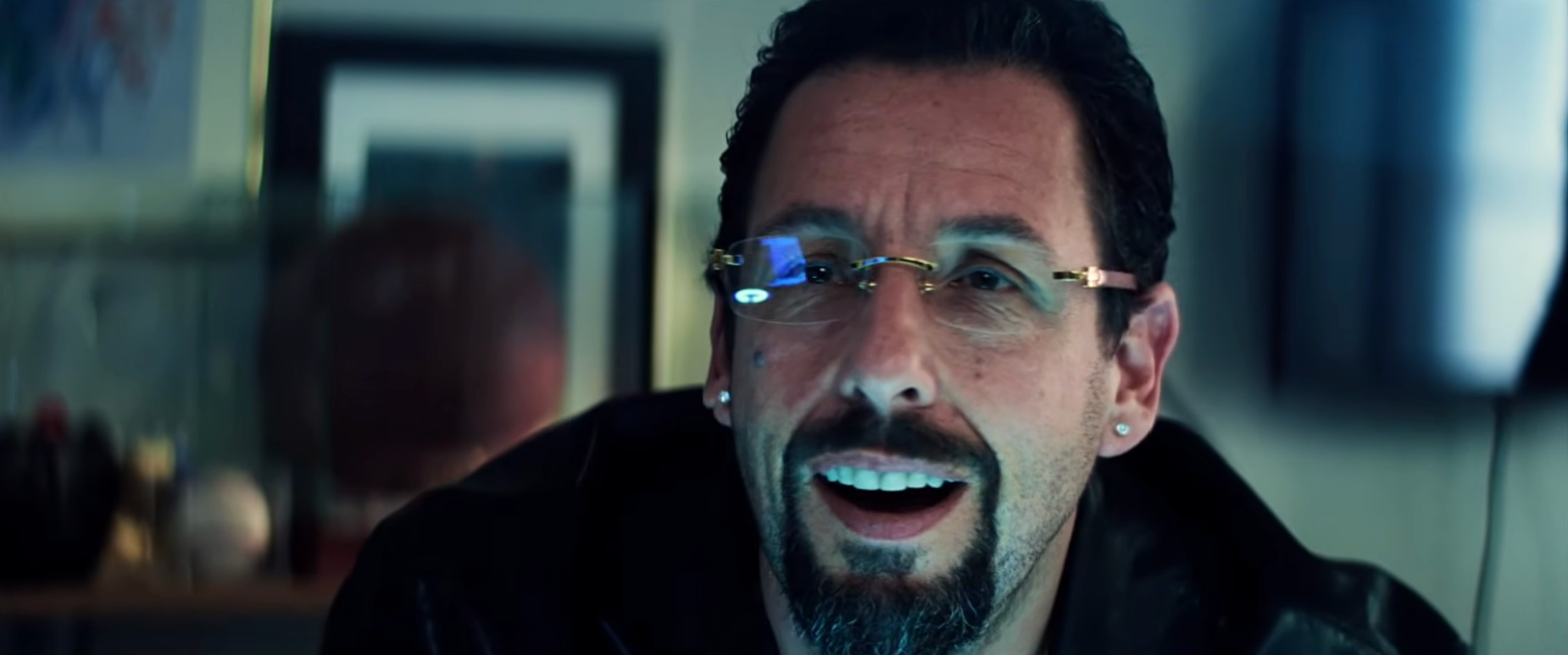 Man with a goatee and glasses, with a surprised expression, in a dimly lit indoor setting
