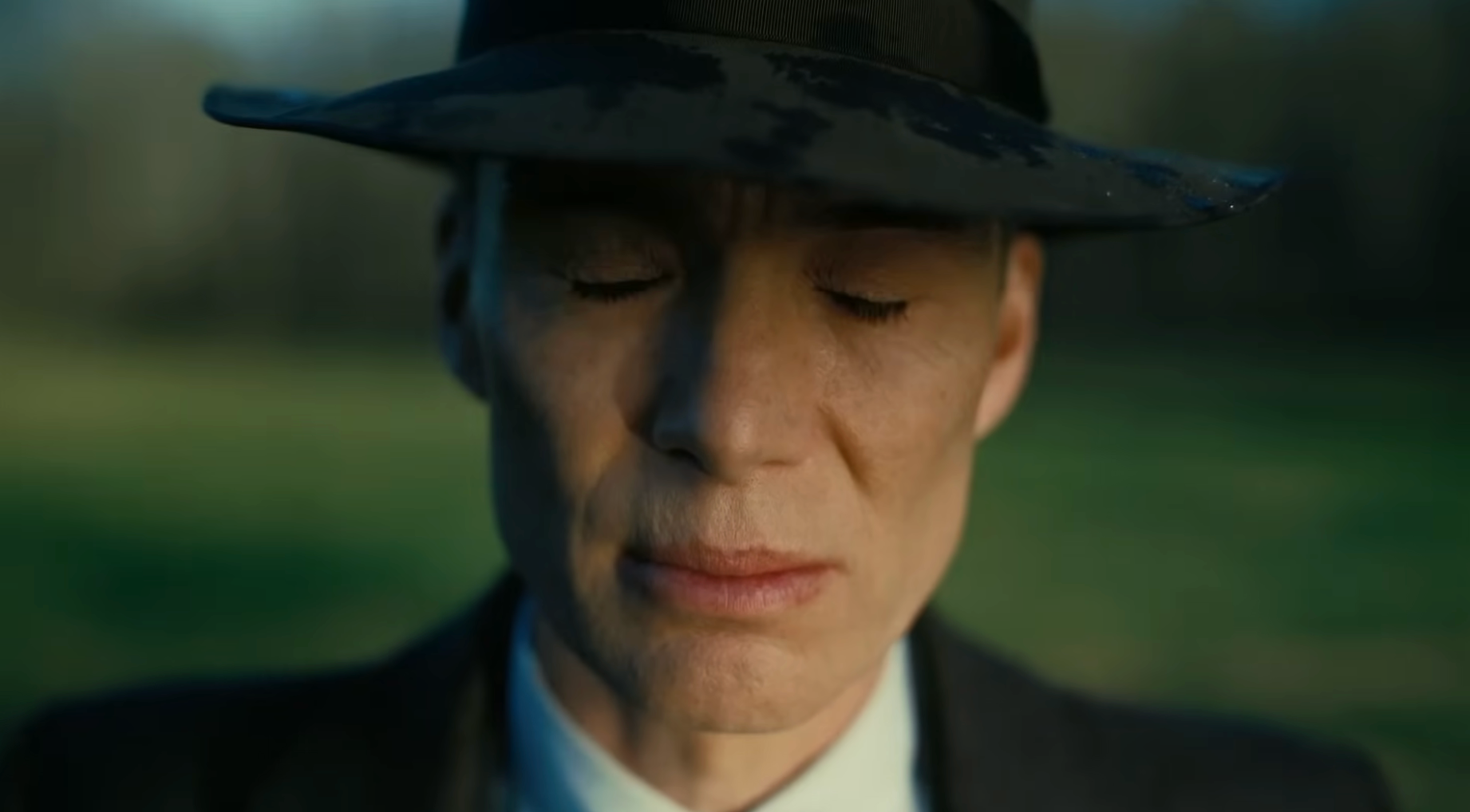 Person in close-up with eyes closed, wearing a wide-brimmed hat and a suit, standing outdoors