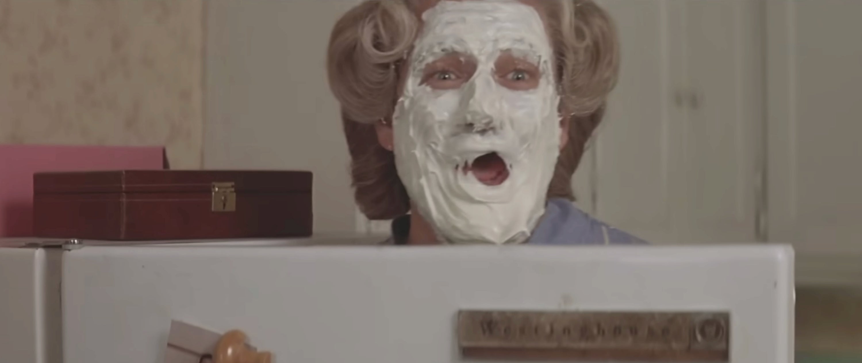 Person with icing-covered face peeking over a refrigerator door, looking surprised