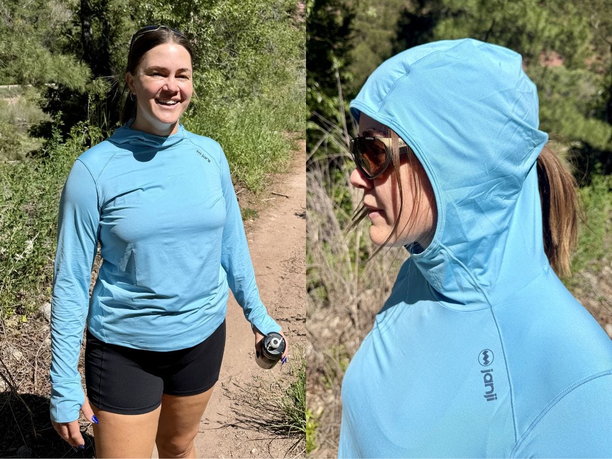 Person wearing a light blue Janji hooded long-sleeve top on a sunny wooded trail, with a close-up hood view.