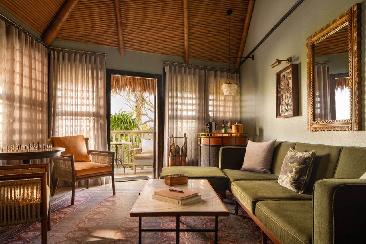 Interior of a tropicalthemed suite with wooden ceiling sitting area and balcony overlooking lush greenery