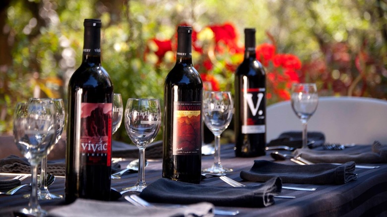 Elegant table setting with bottles of Vivác and branded wine glasses, with black napkins and a natural background.
