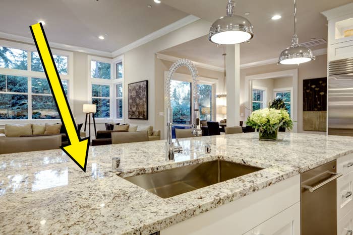 Spacious kitchen with granite counters, a modern faucet, and a vase of white flowers. Open layout leading to a living area with large windows