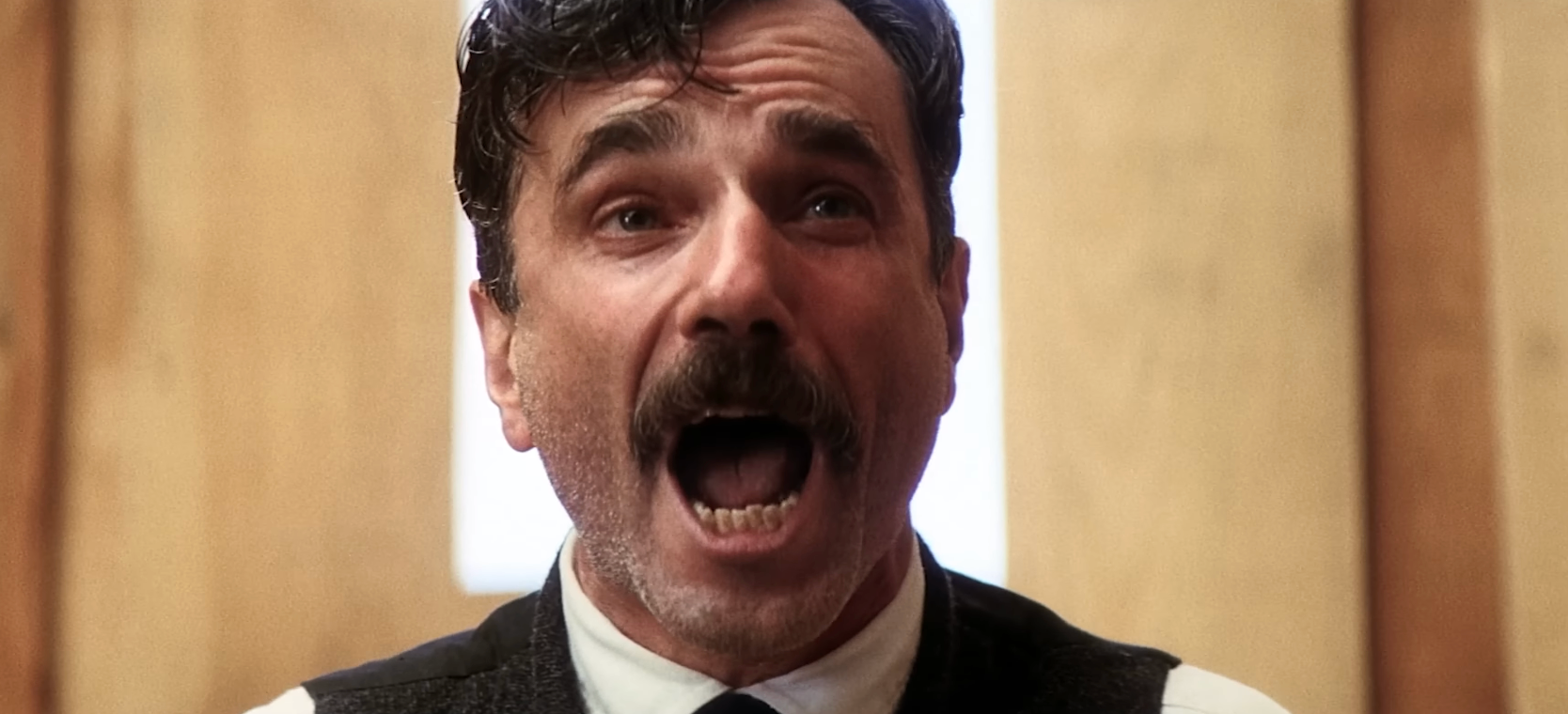 A person with a mustache is dramatically yelling, wearing a formal vest and tie, set against a wooden backdrop
