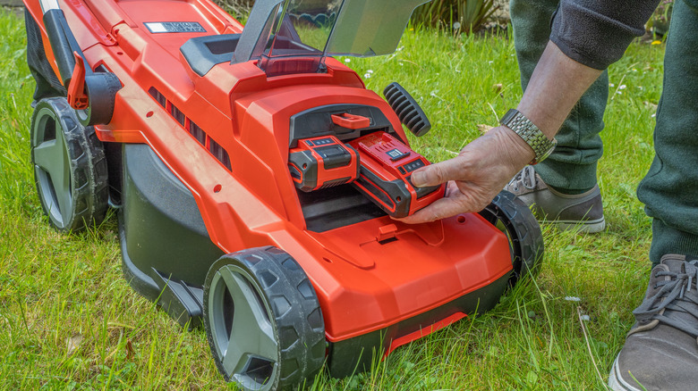 Man changing cordless electric lawn mower batteries