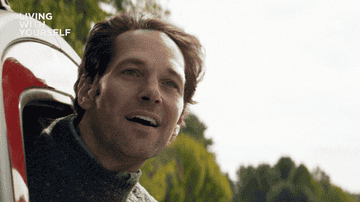 A person leans out of a car window, smiling, with the text "Living With Yourself" in the corner