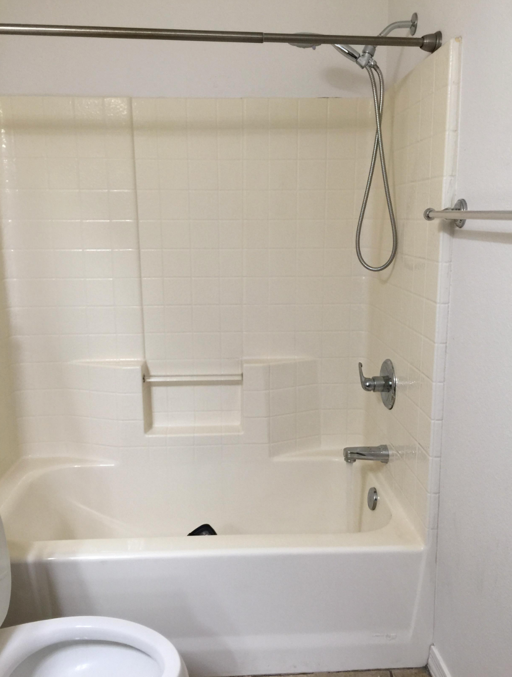 Bathroom with a white bathtub-shower combo, handheld showerhead, and built-in soap shelf