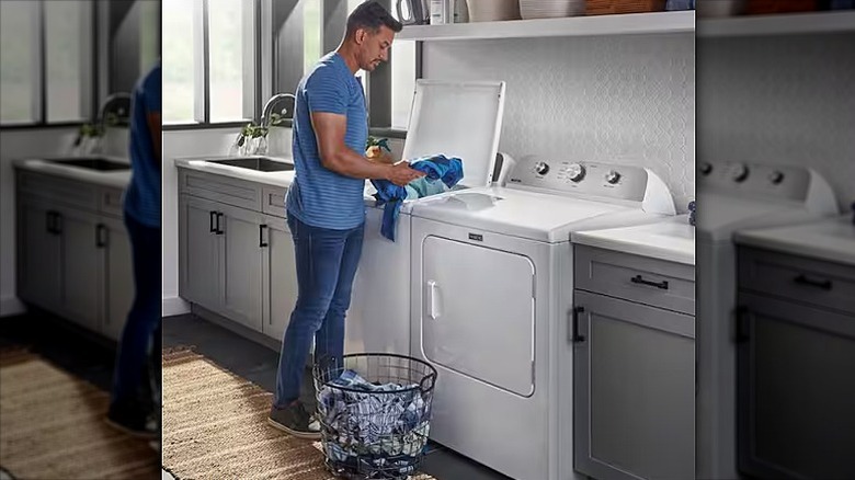 Man loading clothes into a dryer in a laundry room.