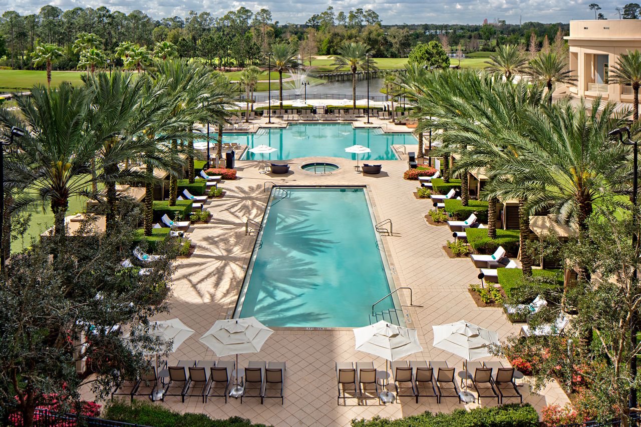Resort with multiple pool sections and lush surroundings viewed from above with lounge seating and palm trees