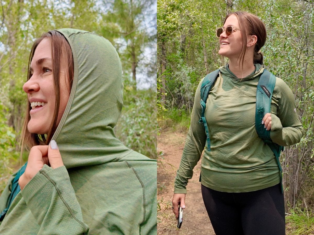 A hiker in a green hooded top and sunglasses stands on a wooded trail with a backpack.