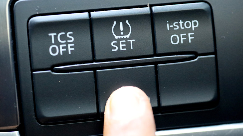 A driver's finger pressing near the TPMS button of a car.