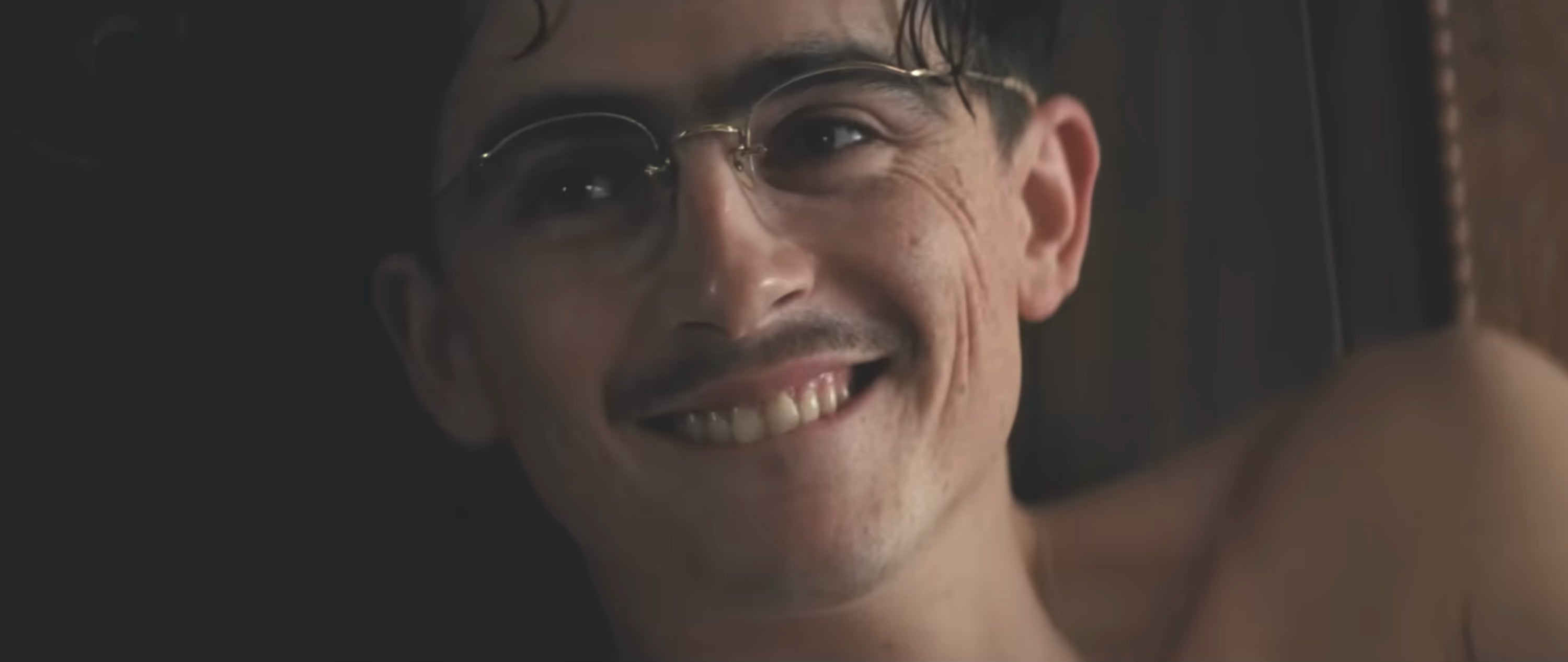 Person smiling with glasses and a small mustache, looking directly at the camera in a relaxed setting