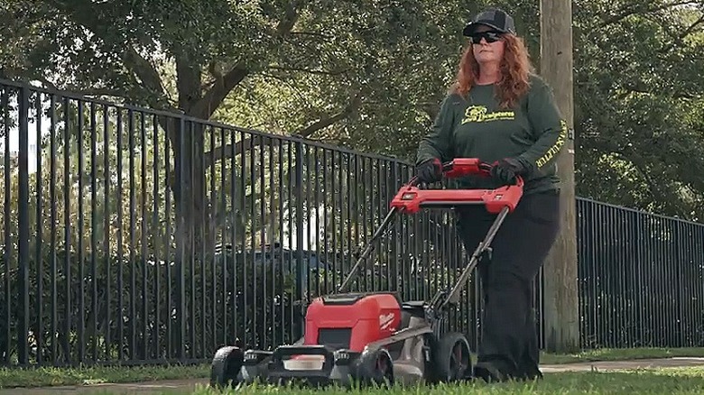 Woman using a walk behind mower in a lawn.