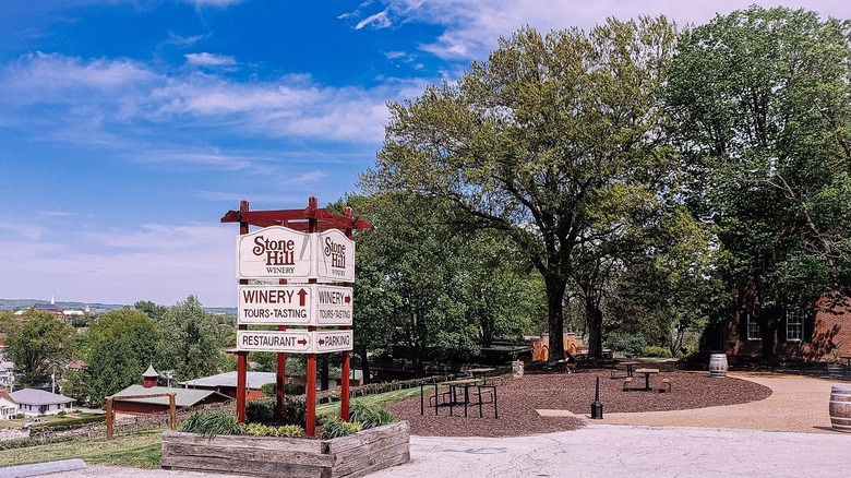 Stone Hill Winery's wooden sign overlooking the town of Hermann with trees and picnic tables in the background.