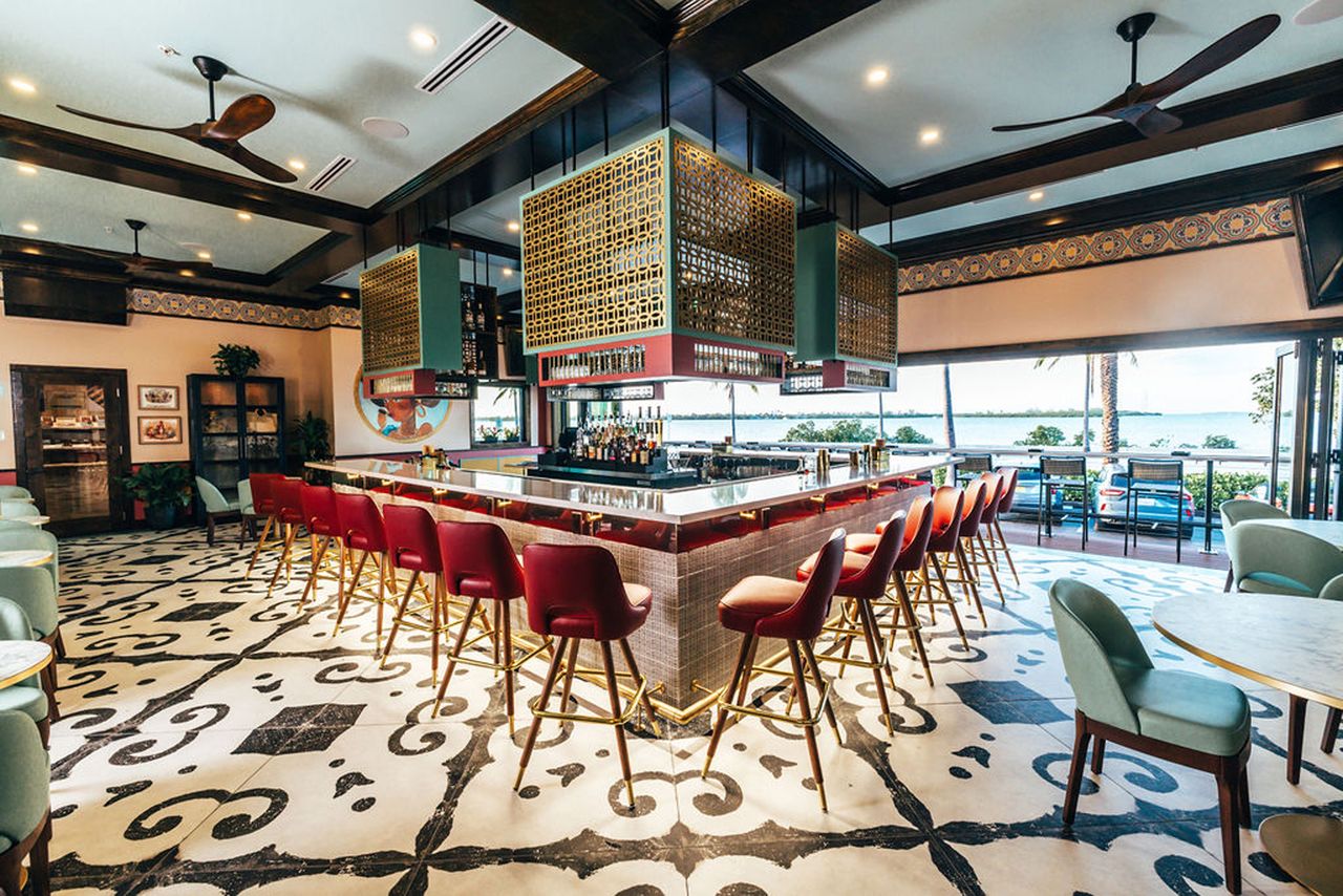 A bar area with barstools and decorative tile flooring featuring rows of liquor bottles and windows providing an outdoor view
