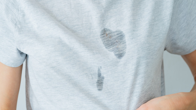 A person wearing a gray T-shirt with two large grease stains on the chest