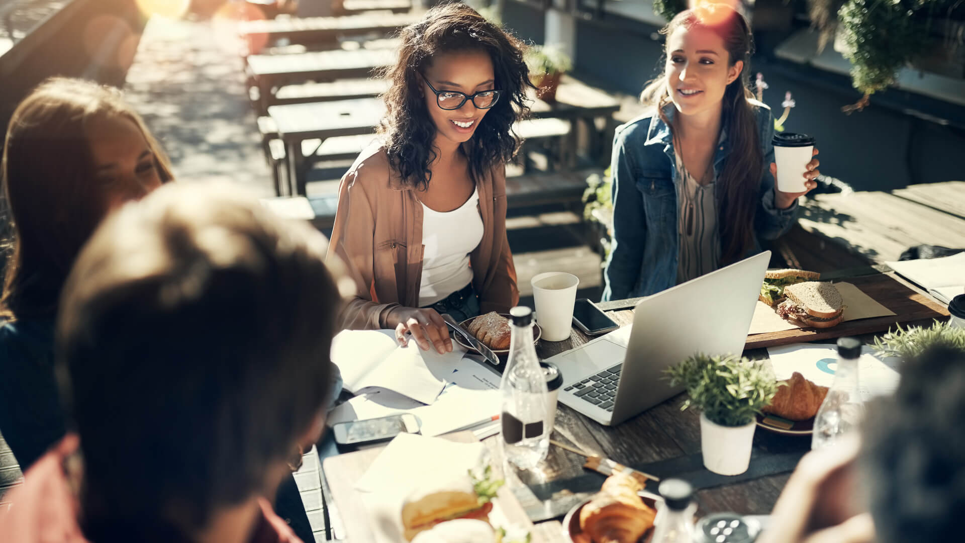 Discover a group of young Gen Z friends eating lunch together while getting work done on laptops outside