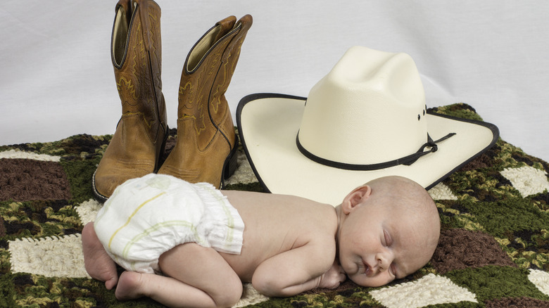 A baby posed with cowboy boots and a hat