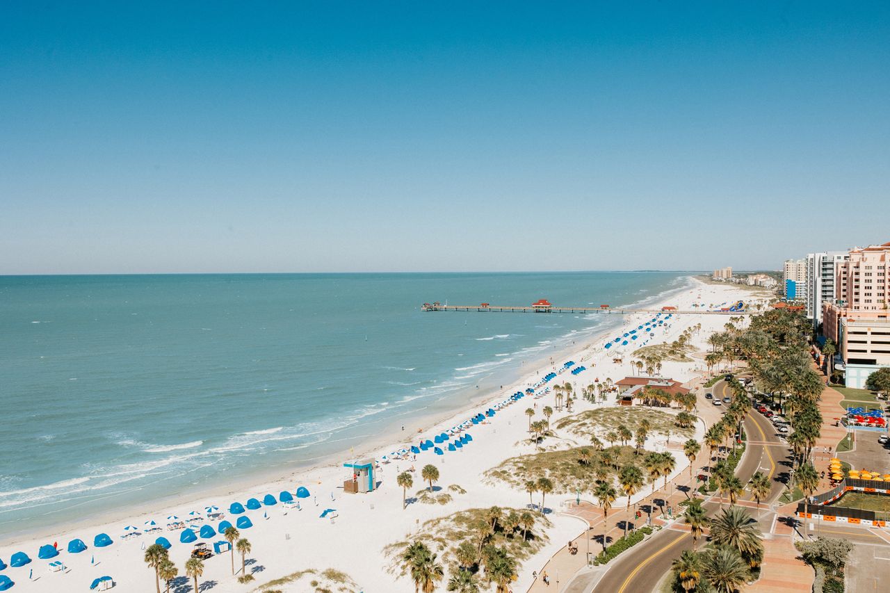 Aerial view of a beach with umbrellacovered lounging areas and adjacent urban buildings along the coastline