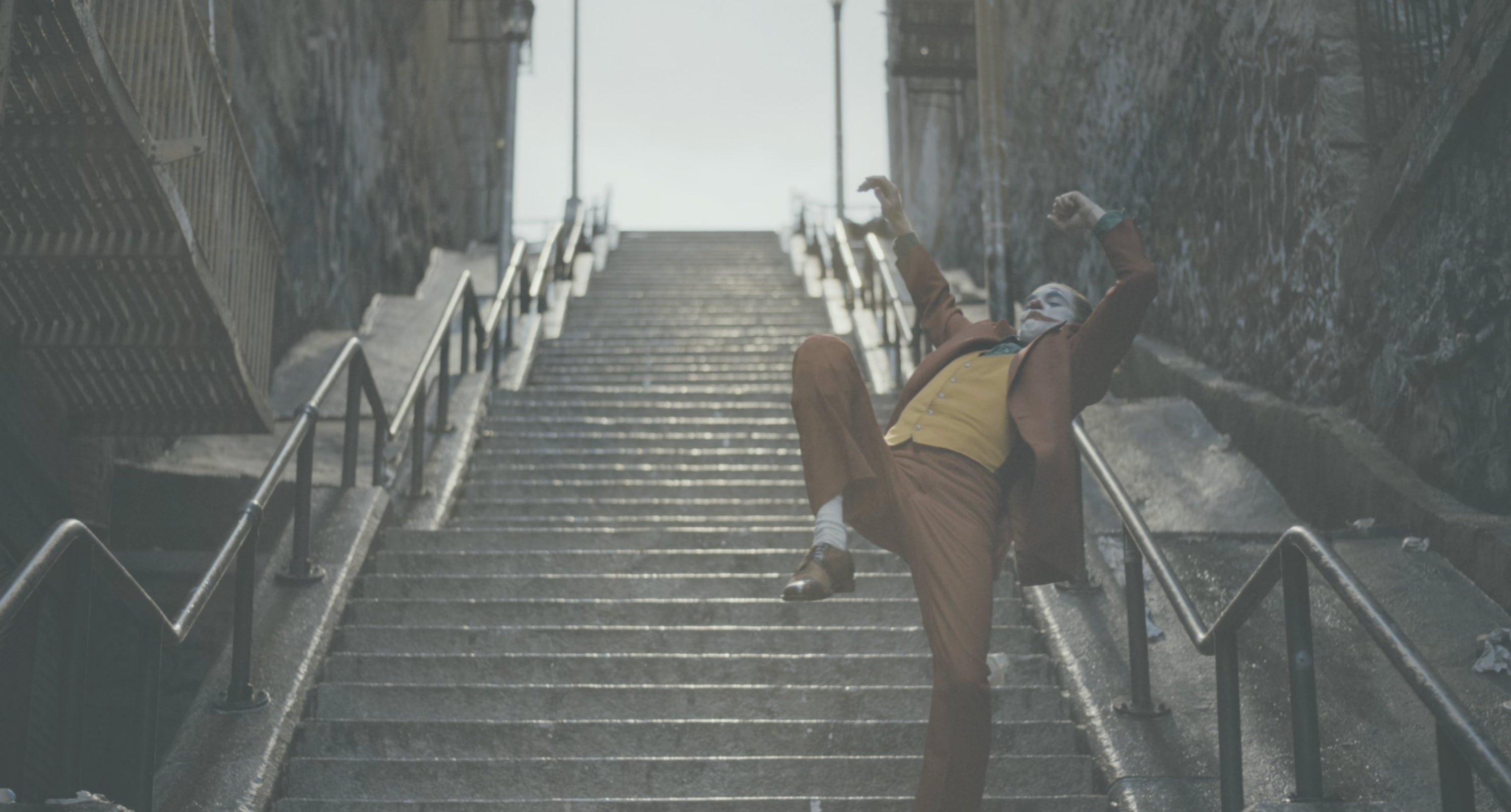 Person in a vintage suit and mask dances dramatically on a city staircase