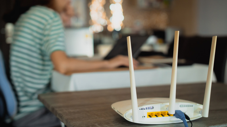 A woman is working from home and a white router is on the table nearby