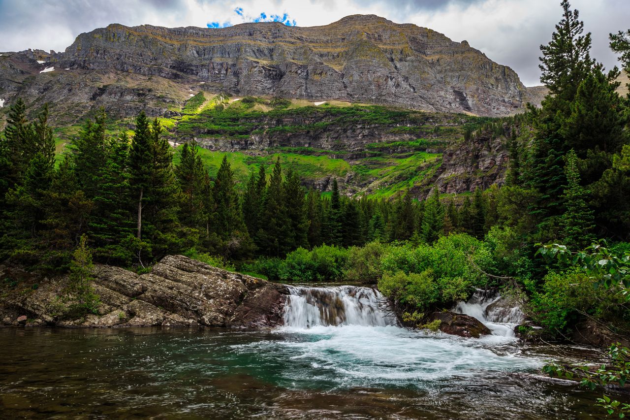 Scenic waterfall and forest with mountain backdrop in Glacier National Park